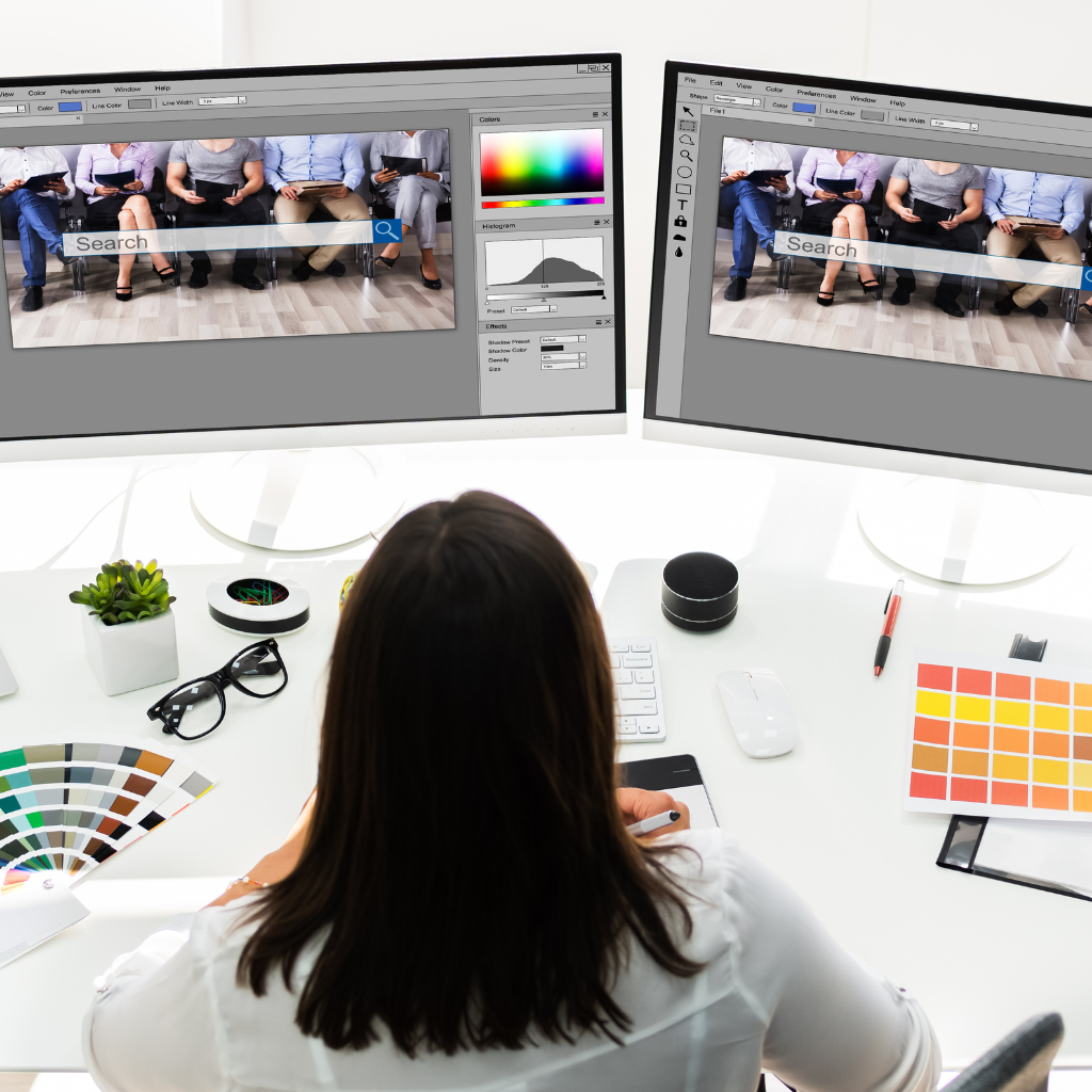 simply the best digital marketing graphic design photo of woman in white sitting at a white desk in front of two monitors showing graphic design content