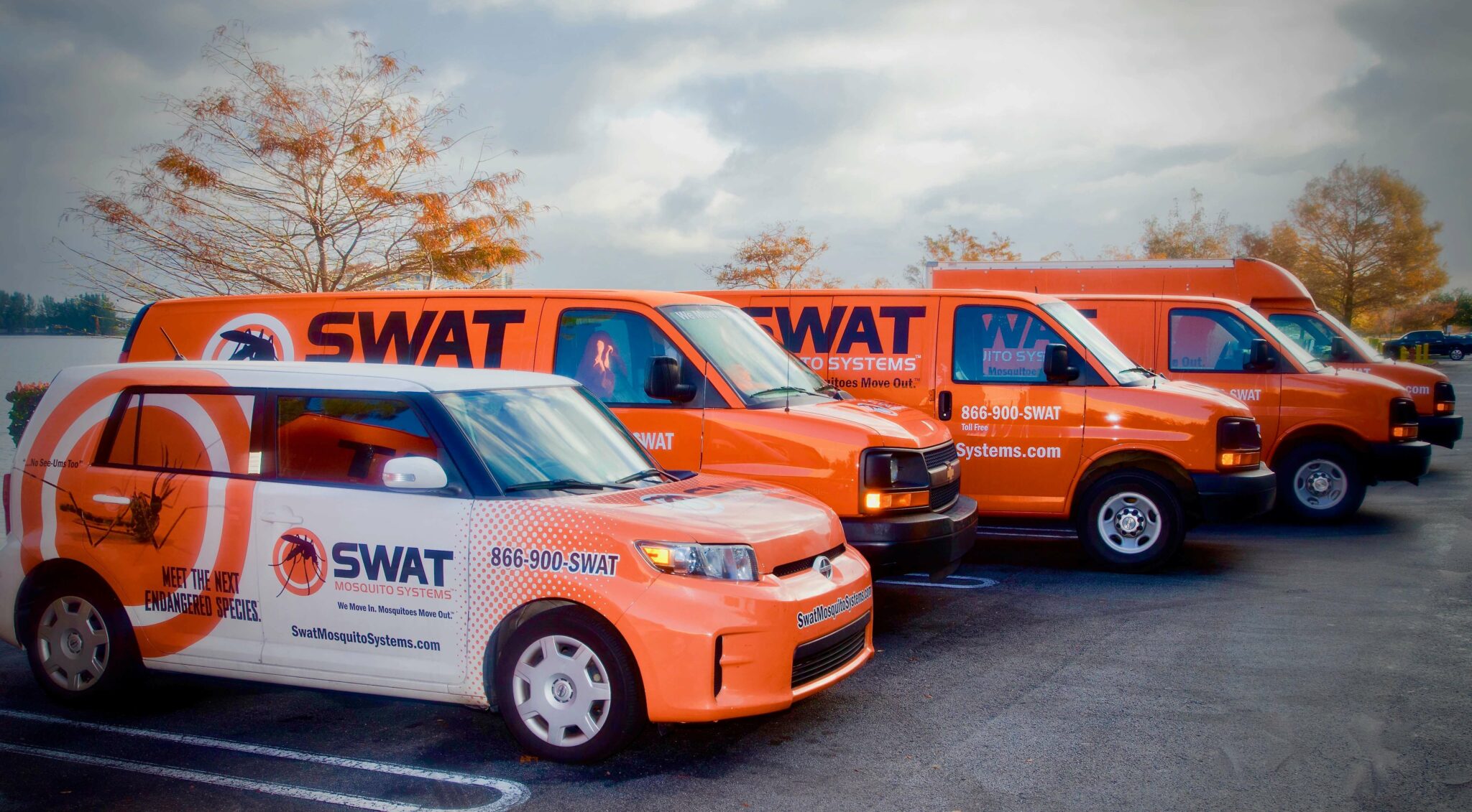 five orange swat mosquito misting trucks parked next to each other