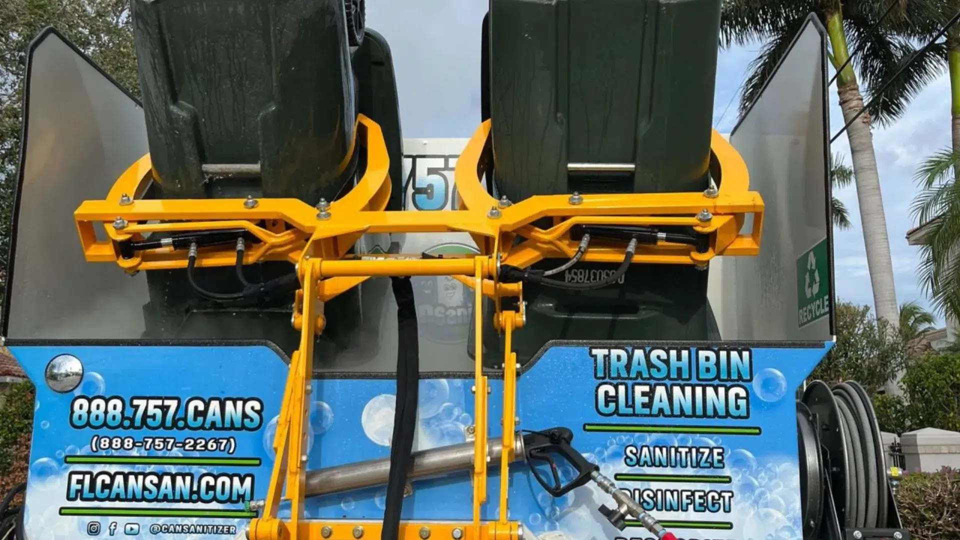 Automated trash bin cleaning system in action, lifting two garbage cans for sanitization.